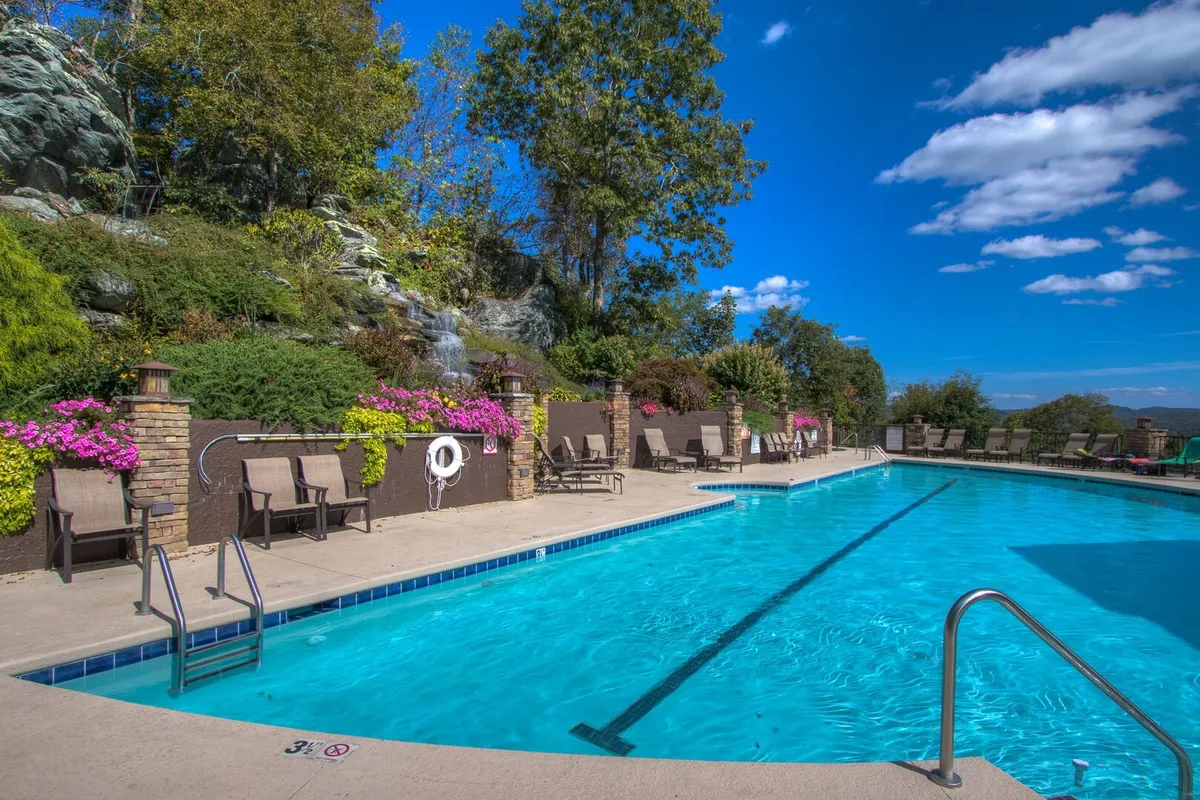 An inviting outdoor swimming pool surrounded by rocky landscaping, blooming flower beds, and comfortable lounge chairs. The area is well-designed for relaxation, swim time, and social gatherings, appealing to family fun and leisure.