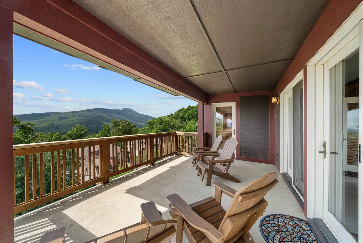 A spacious wooden deck is furnished with comfortable Adirondack chairs, inviting guests to relax while taking in sweeping mountain views. A decorative mat adds warmth and style, while the tranquil outdoor setting is perfect for enjoying morning coffee or evening stargazing.
