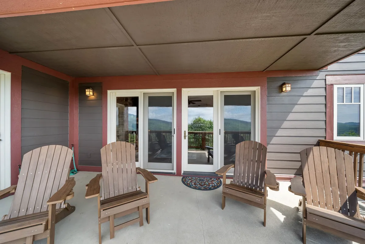 This exterior image features a welcoming outdoor seating area with Adirondack chairs arranged around double glass doors, accented by a decorative rug. The setting invites guests to relax, enjoy the fresh mountain air, and gather for casual conversations or celebrations. The view hints at scenic sunrises and sunsets over the hills, perfect for group activities or unwinding after a day of adventure.
