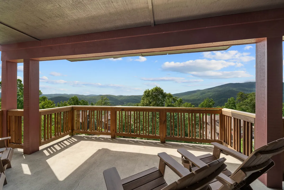 A wooden deck features cozy deck chairs facing out toward a panoramic mountain view. The natural landscape and early morning or late evening light create a peaceful, romantic atmosphere ideal for a couples’ escape.