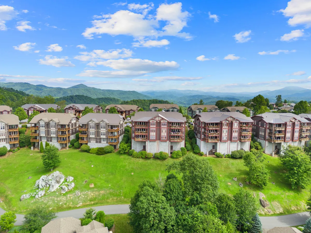 A sweeping exterior view of multi-story buildings set against a lush green lawn and a dramatic mountain backdrop. The open space offers a sense of freedom and connection to nature, with visible trails and ample room for outdoor activities.
